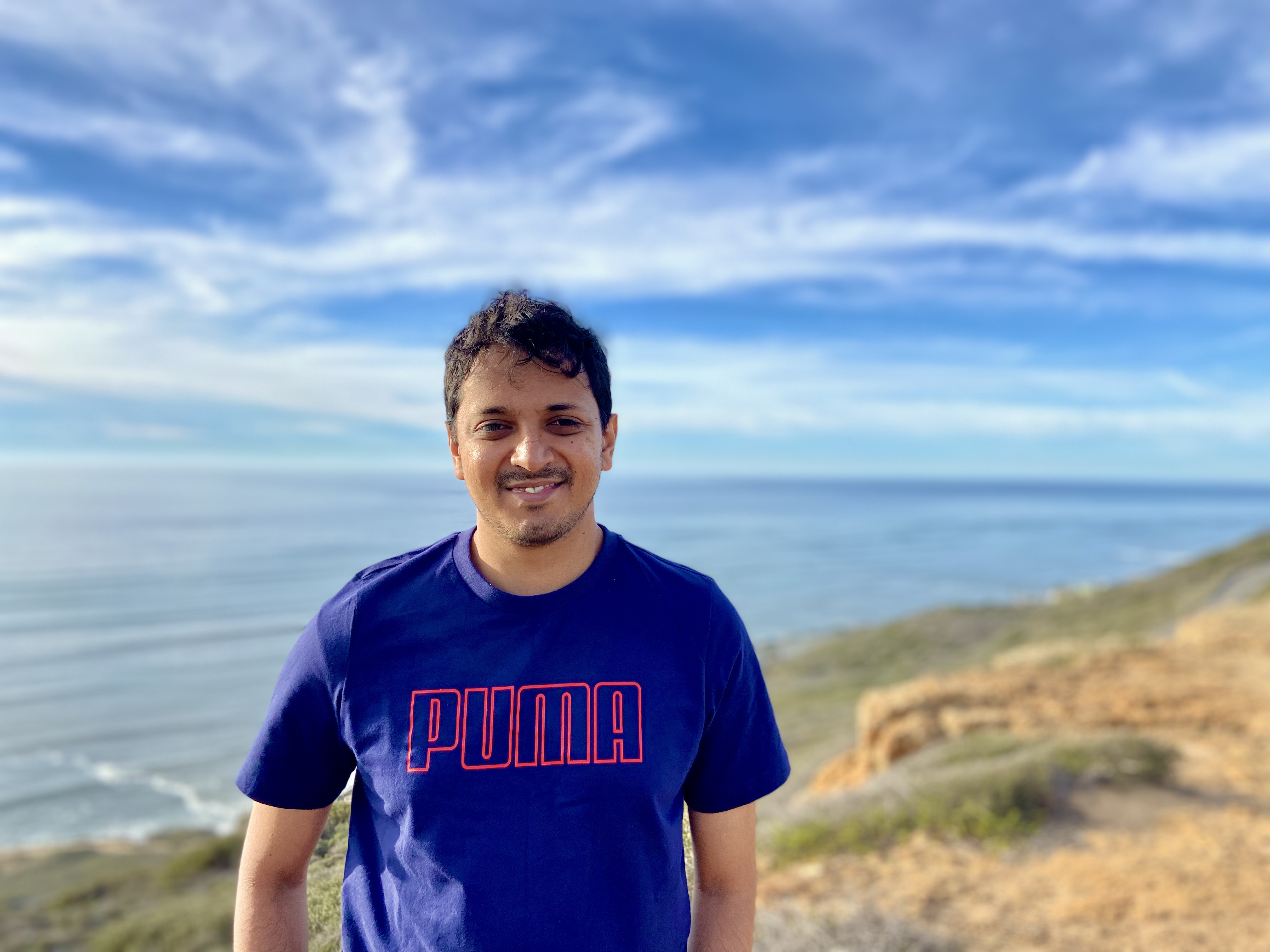 Vaishnav wearing a blue shirt against the backdrop of a blue sky and the pacific ocean.